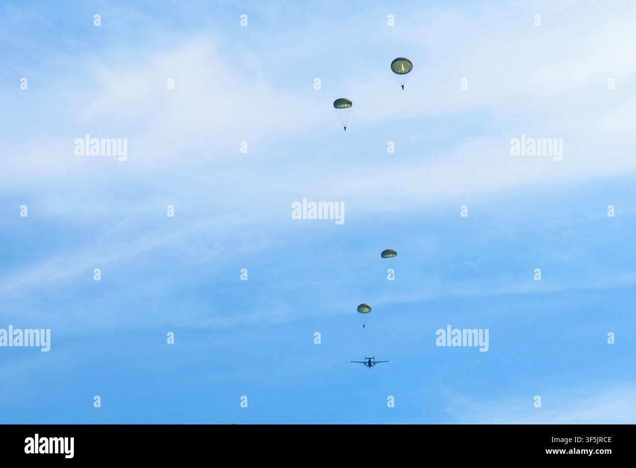Una fotografia diurna che cattura quattro paracadutisti che scendono attraverso un cielo blu brillante con nuvole leggere. Gli individui sono sospesi sotto parapendii aperti, o Foto Stock
