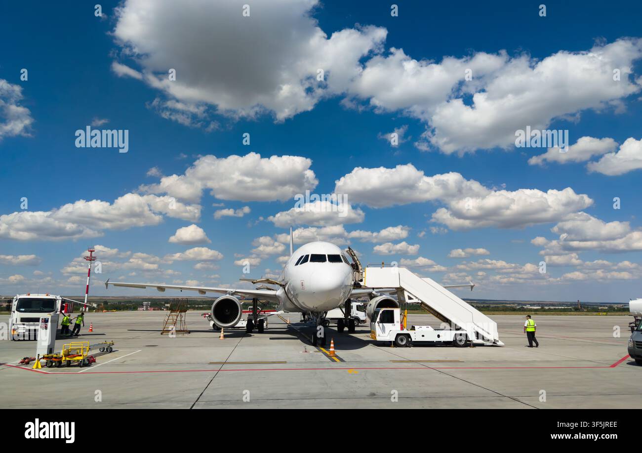 Una vista frontale di un aereo passeggeri commerciale bianco parcheggiato su una pista di cemento di un aeroporto in una giornata luminosa e soleggiata. Un veicolo scale di imbarco mobile è Foto Stock