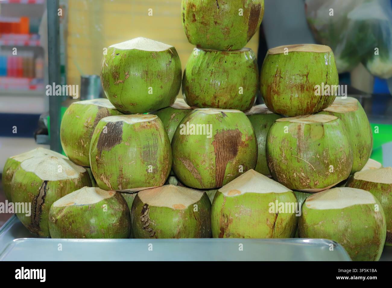 Giovani noci di cocco fresche e aromatiche impilate a piramide su un bancone di metallo in un mercato di frutta di strada thailandese locale, pronte per un rinfresco tradizionale. Foto Stock
