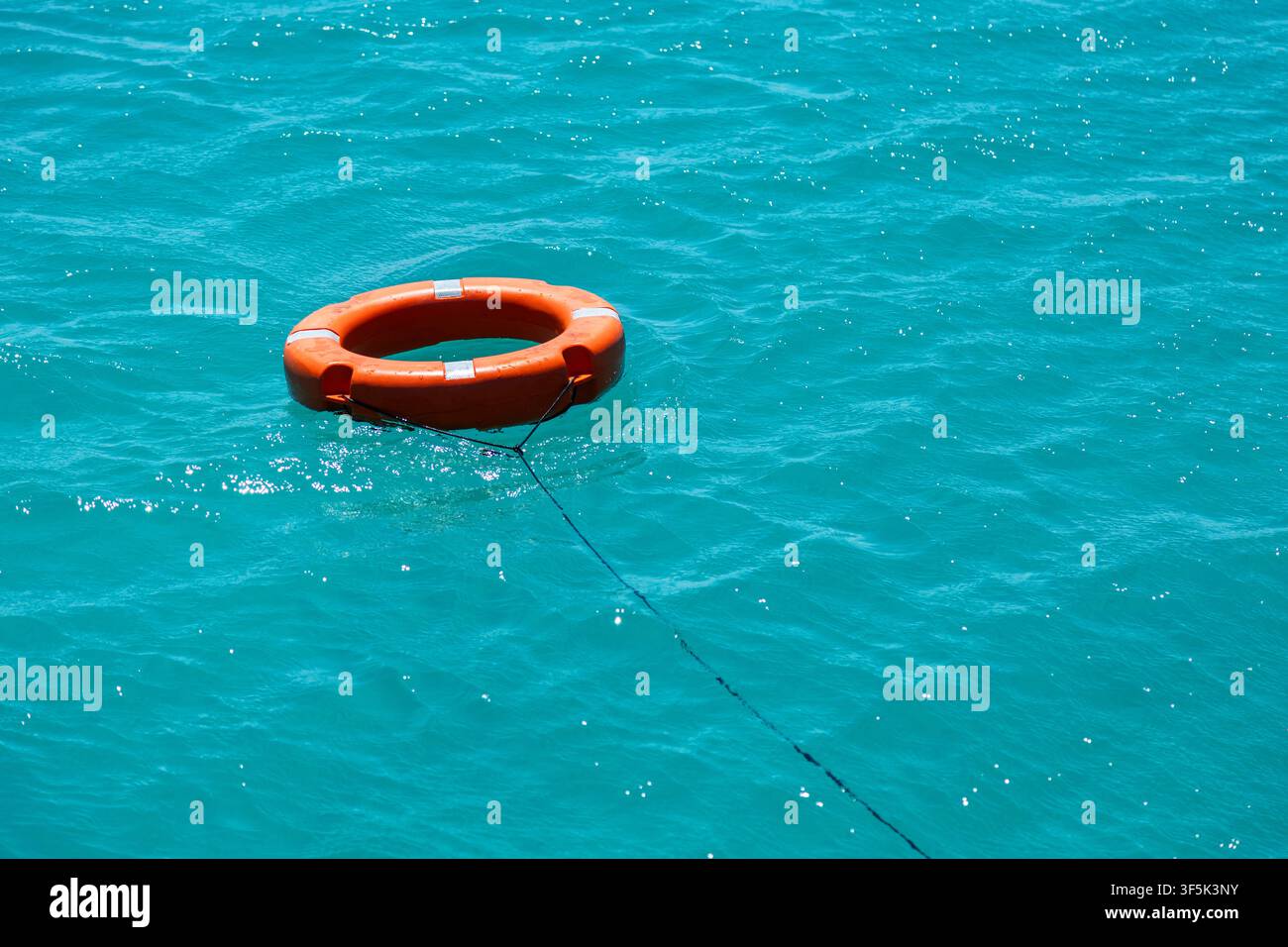 Boia di salvataggio arancione brillante attaccata a una corda di sicurezza che galleggia su acqua di mare turchese chiara, creando uno sfondo vivace di sicurezza marina e vacanze estive Foto Stock