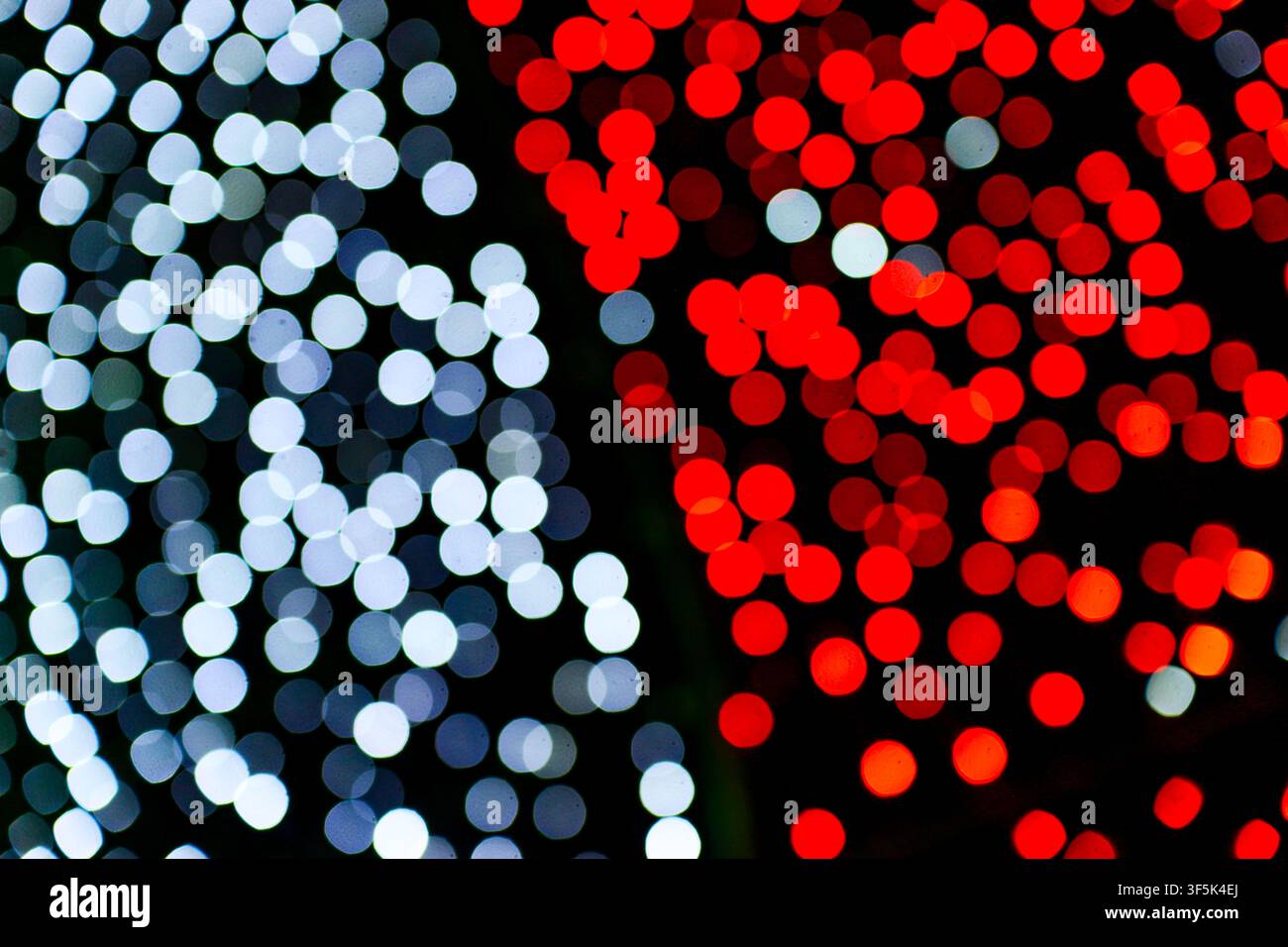 Sfondo bokeh astratto a tono doppio con luci circolari rosse e bianche sfocate che brillano su uno sfondo nero notturno. Foto Stock