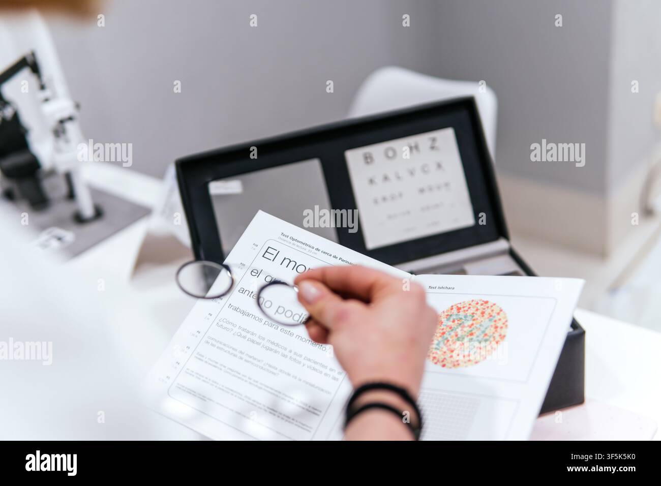 Primo piano di una donna che usa una lente d'ingrandimento per esaminare una tabella della vista accanto a attrezzature ottiche in un negozio di ottica, rappresentando un test della vista, occhio Foto Stock