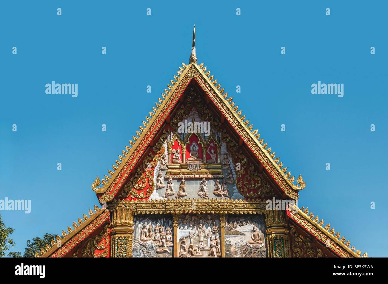 Dettaglio del tetto dorato e ornato del tempio Wat Si Muang a Vientiane, Laos, con figure buddiste scolpite, frontoni rossi e pinnacoli decorativi sotto un cl Foto Stock