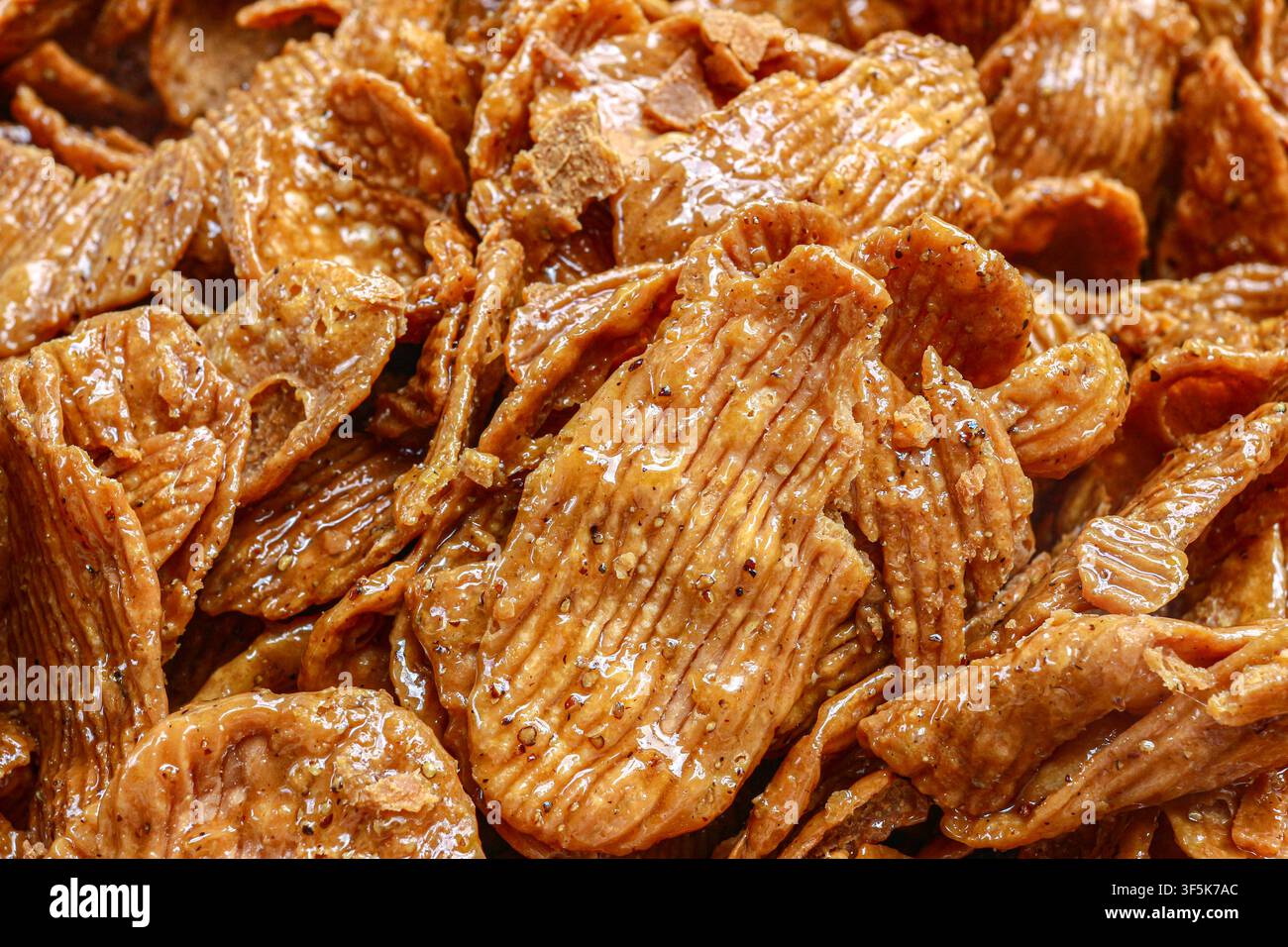 Macro estremo di patatine thailandesi glassate al caramello croccanti (khrongkhraeng krop) con pepe sbriciolato, sfondo in texture alimentare marrone dorato. Foto Stock