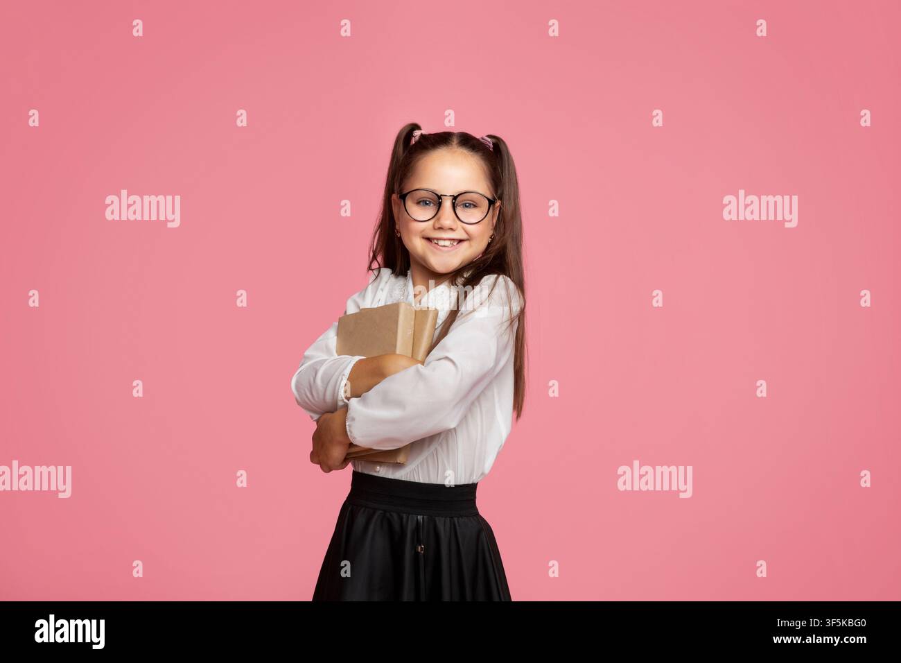 Amo la scuola. Sorridente ragazza con in occhiali abbraccia libri e guarda la macchina fotografica Foto Stock