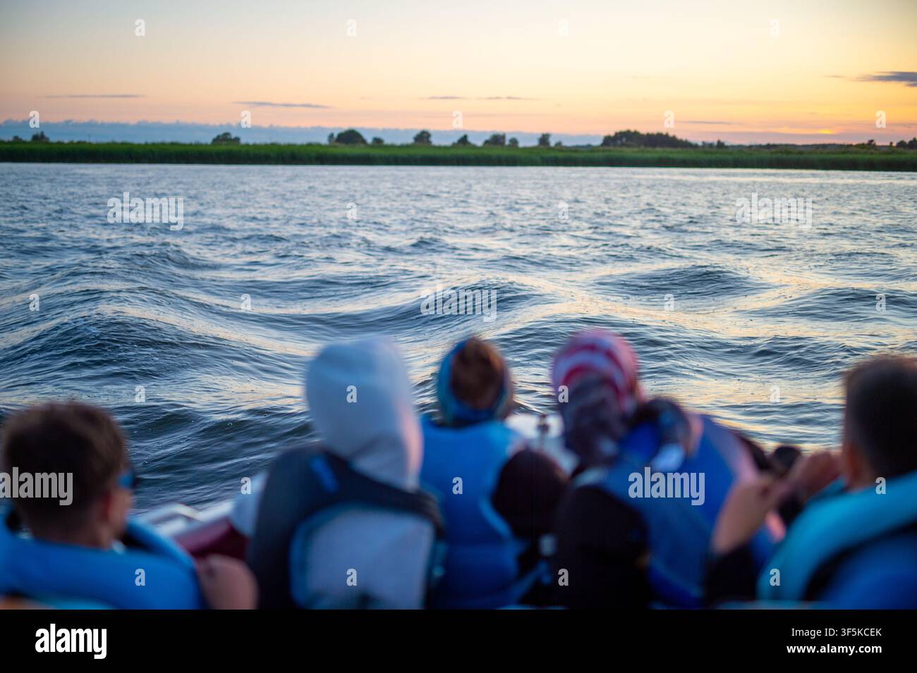 Vista posteriore di passeggeri che si godono una gita in motoscafo su un lago ondulato al crepuscolo Foto Stock
