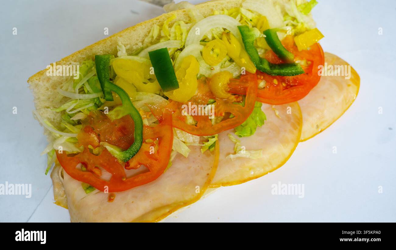 Un panino viene preparato in una gastronomia. Comprende strati di lattuga, pomodori, peperoni verdi, cipolle e fette di carne. Il pane è fresco e la parte superiore Foto Stock