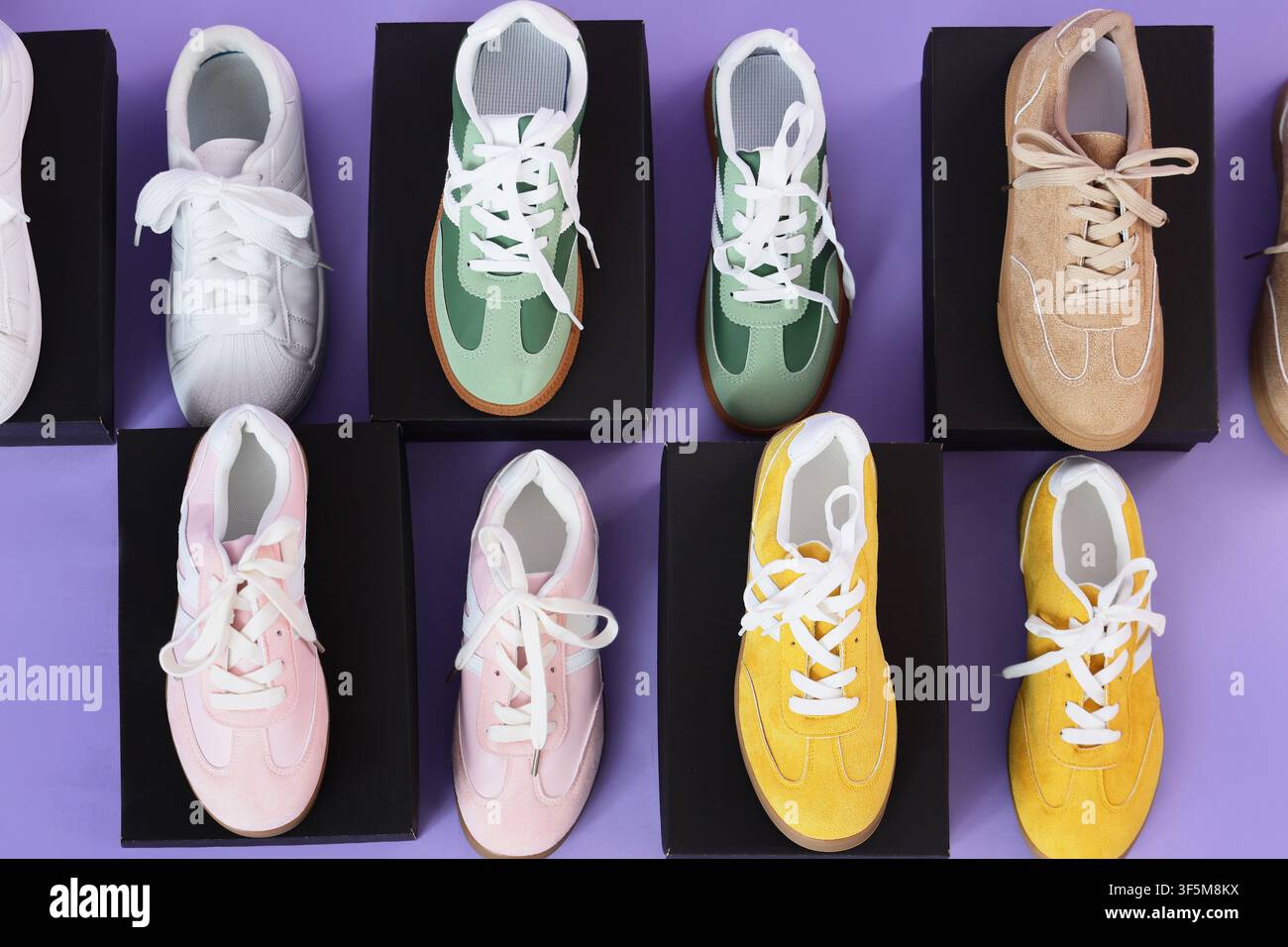 Scarpe da ginnastica colorate su scatole nere con sfondo viola Foto Stock