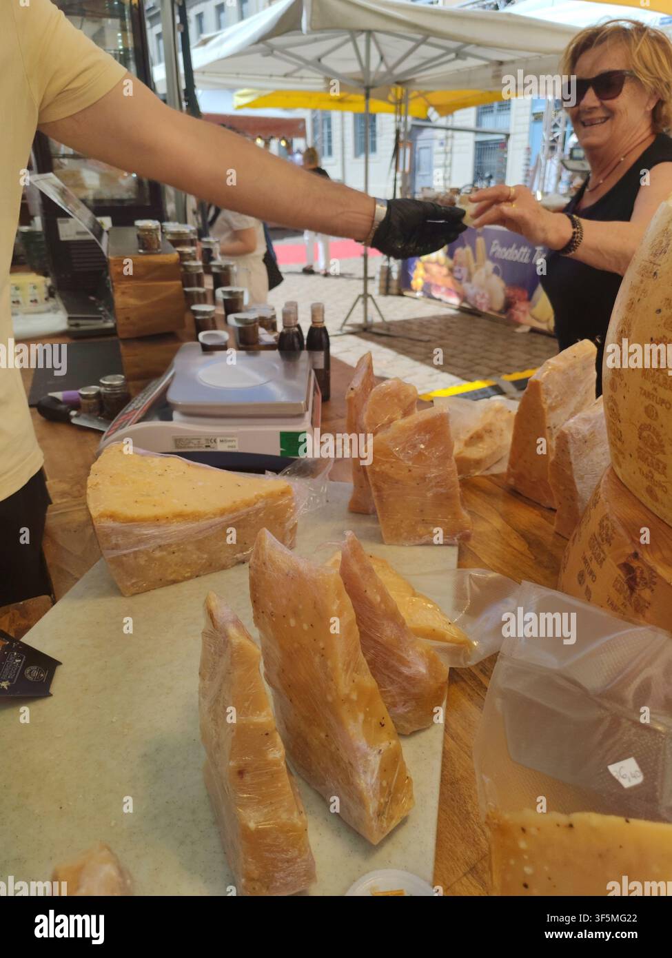 Lione, Francia - 5 giugno 2026: Donna sorridente che assaggia formaggio artigianale al tartufo offerto da un venditore al mercato locale dei contadini, esperienza gastronomica Foto Stock