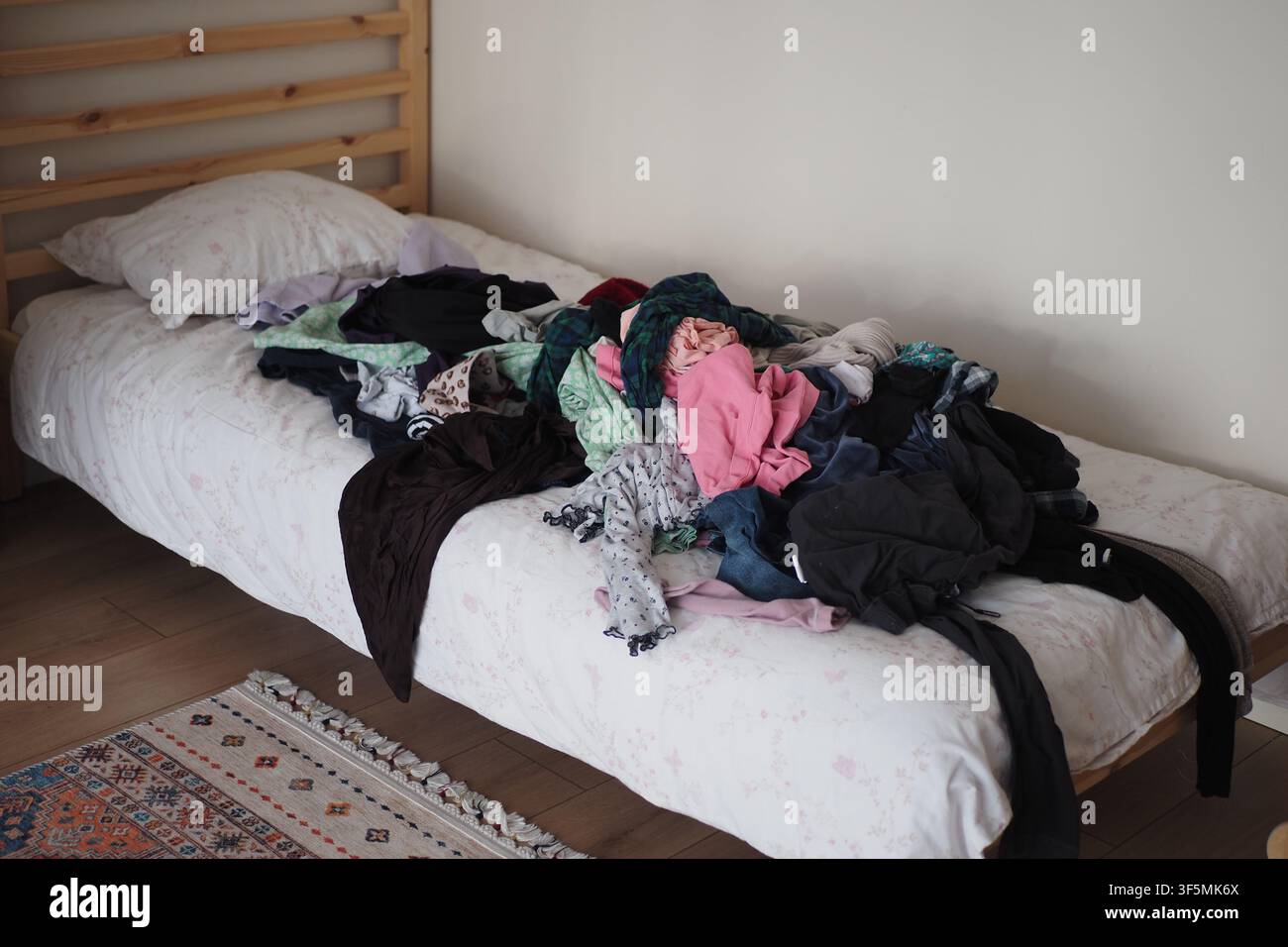 Letto disordinato con vestiti ammucchiati sopra durante il giorno Foto Stock