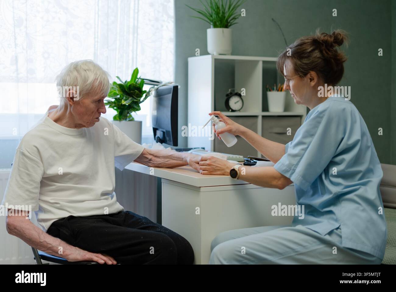 Infermiera che tratta malattie della pelle e applica medicina sul braccio di un uomo anziano in ambulatorio medico. Paziente anziano che riceve cure dermatologiche complete da un professionista sanitario durante una procedura in clinica Foto Stock