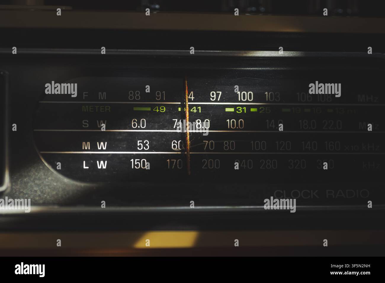 Vista macro ravvicinata di un display di sintonizzazione radio analogico con numeri di frequenza e indicatore dell'ago evidenziati da un raggio di sole in uno stile retrò caldo Foto Stock