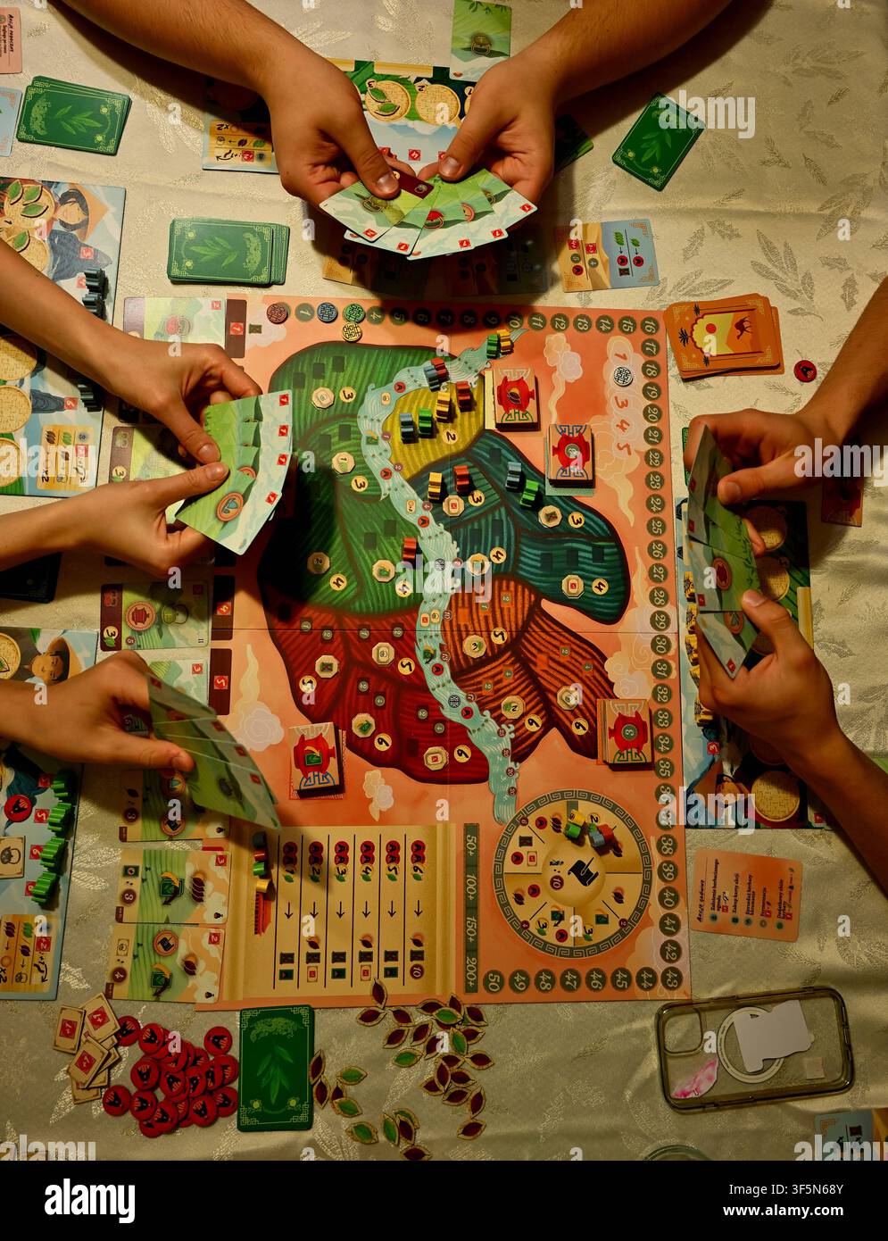 Amici che giocano insieme a un colorato gioco strategico da tavolo intorno a un tavolo con carte e gettoni Foto Stock