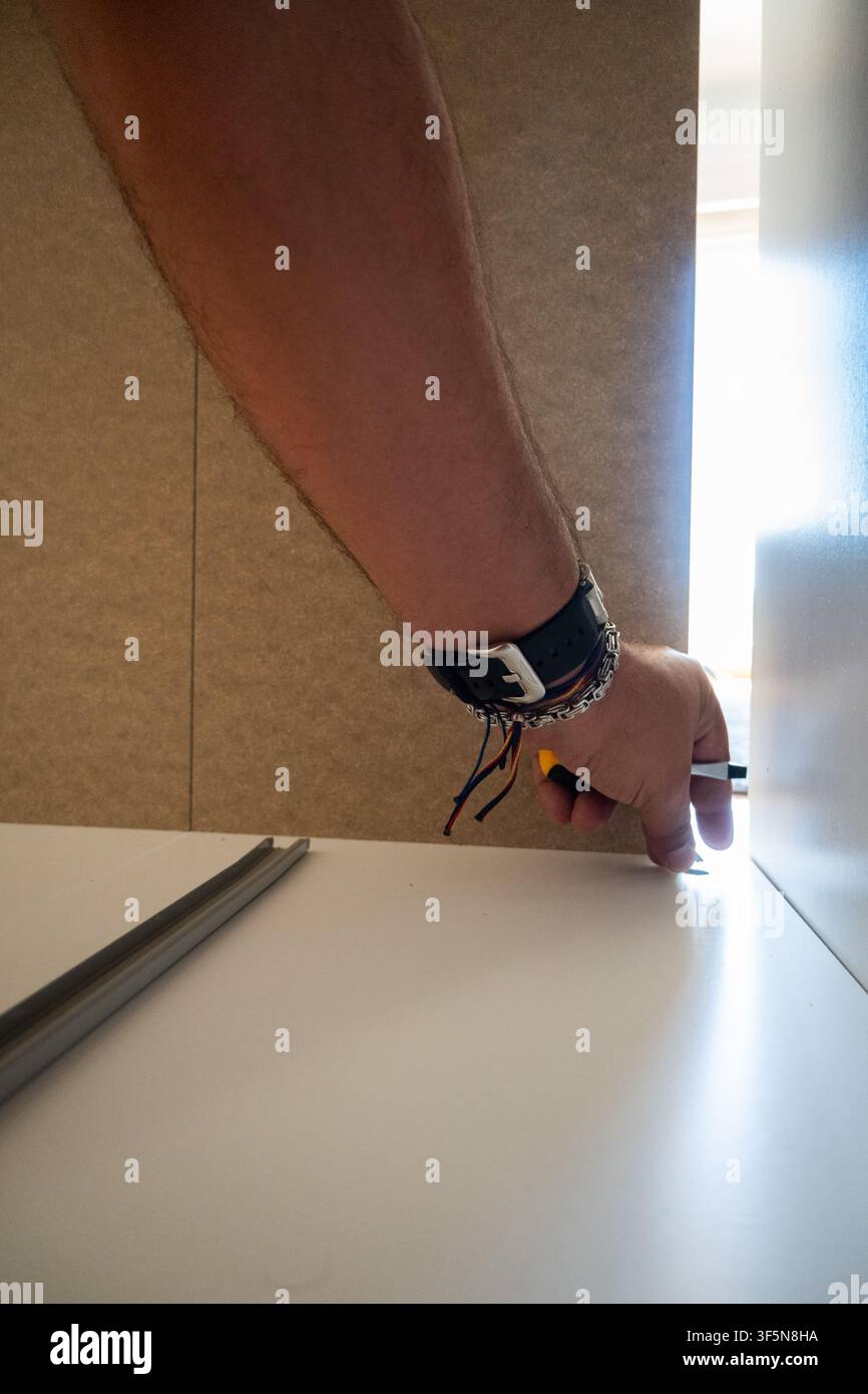 Uomo adulto che assembla parti di mobili bianchi con un cacciavite, costruendo una nuova decorazione per la casa Foto Stock