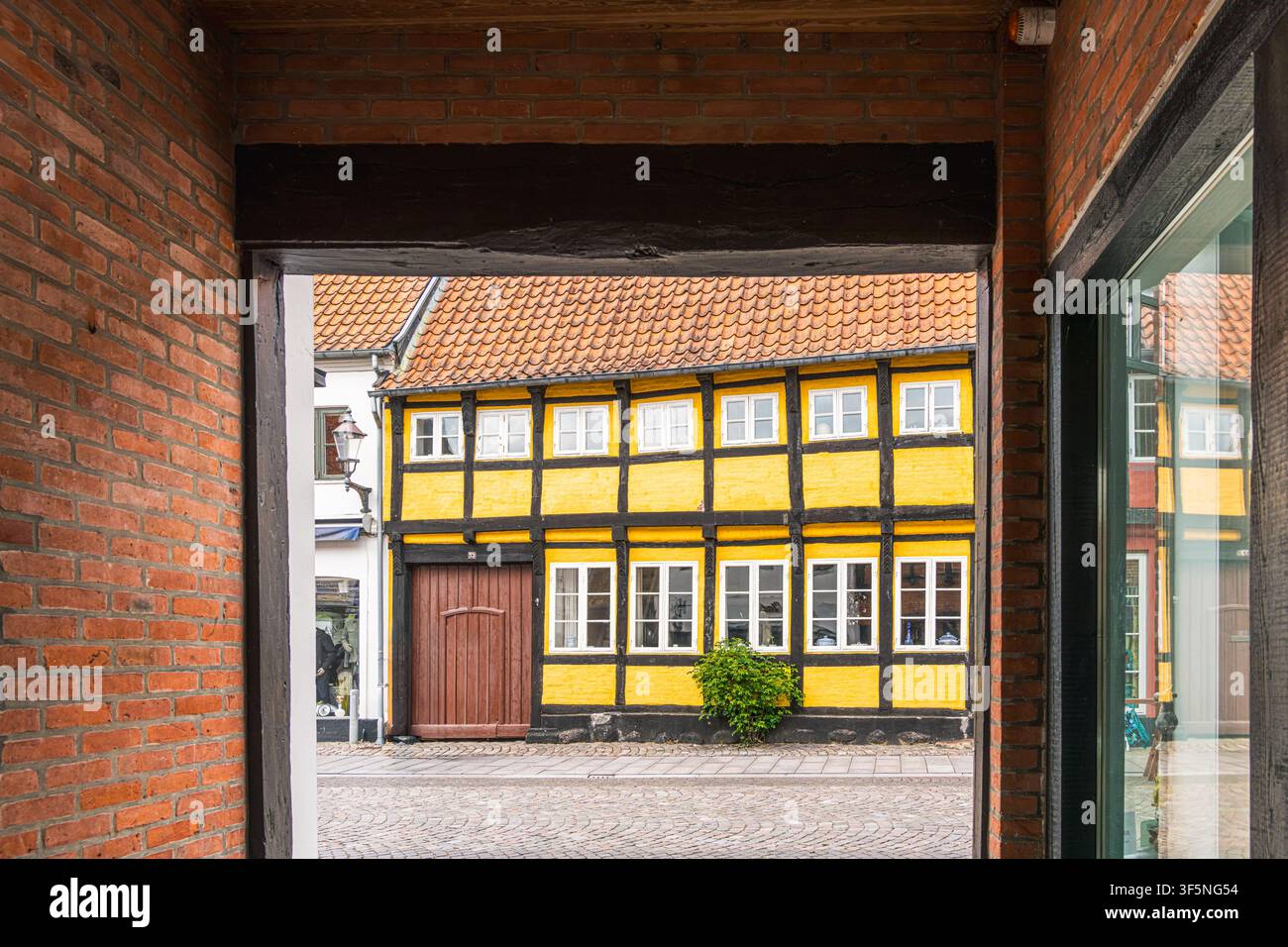 L’eredità in legno incorniciata appare oltre un passaggio in mattoni, rivelando un’architettura a graticcio gialla e nera a Ribe per la storia locale, viaggi danesi Foto Stock