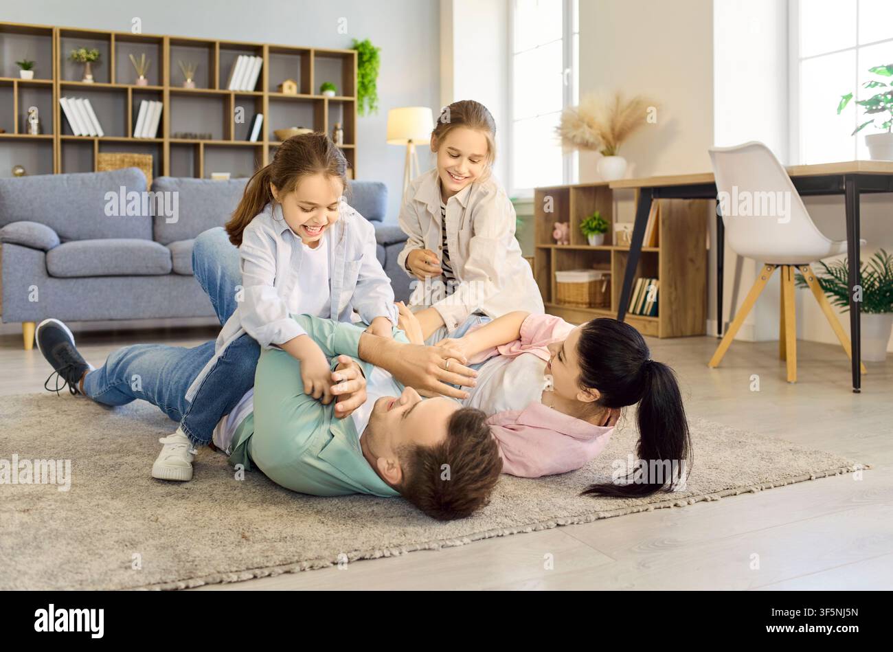 Famiglia felice che si fa il solletico sul pavimento del soggiorno, genitori e figlie che ridono Foto Stock