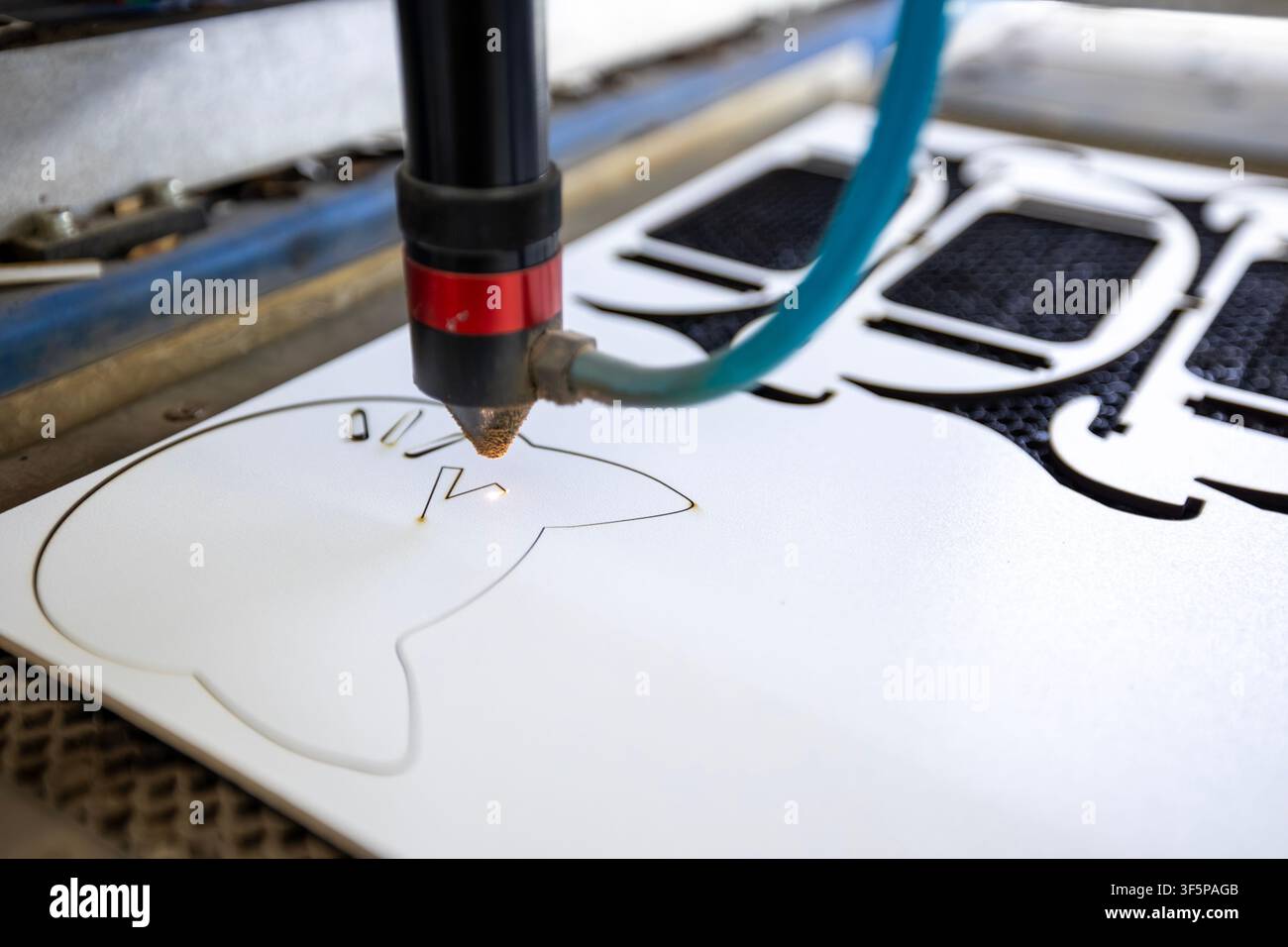 Macchina da taglio laser CNC che crea forme intricate di gatti su una superficie bianca utilizzando una tecnologia di fascio precisa in una moderna officina industriale con metallo ma Foto Stock