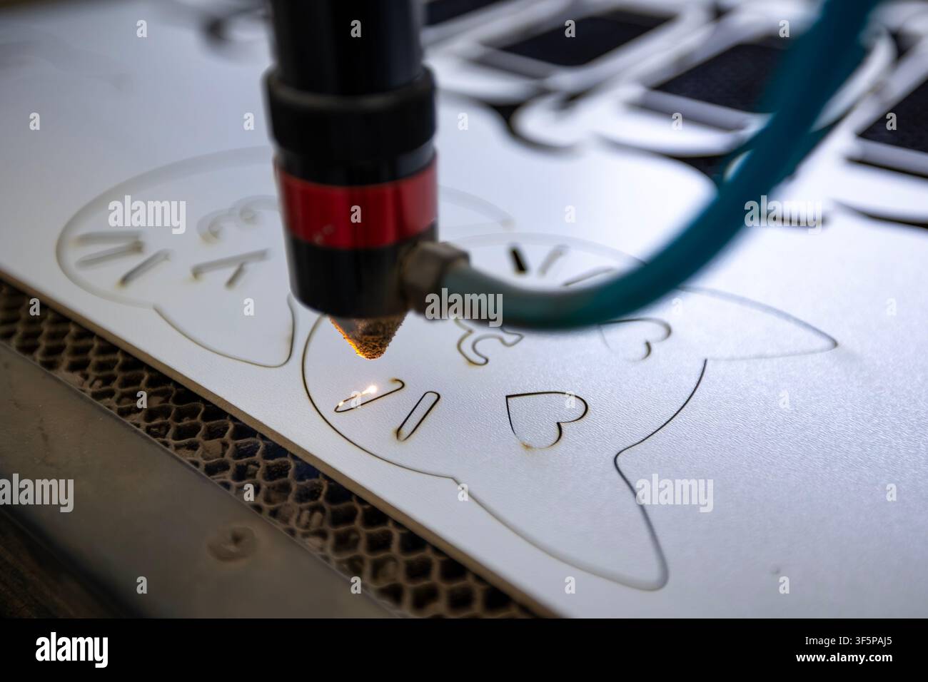 Macchina da taglio laser CNC che incide un motivo a gatto su un foglio di plastica bianco con una ugello di precisione e un raggio intenso in un ambiente di officina con automazione Foto Stock
