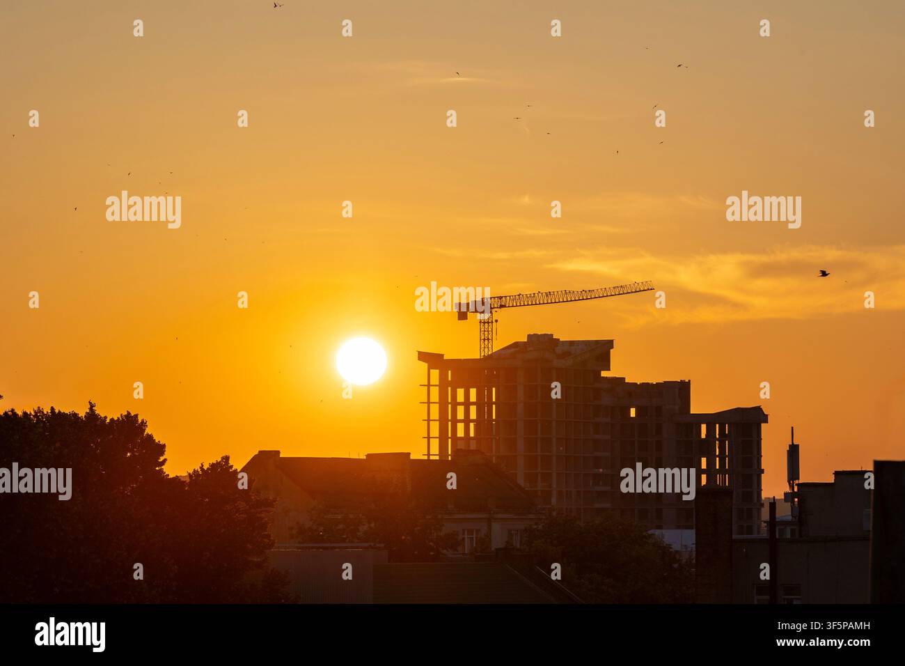 Ternopil, città ucraina tramonto cantiere edile e silhouette di una gru contro un cielo arancione, architettura residenziale, edifici urbani, alberi rigogliosi, vas Foto Stock