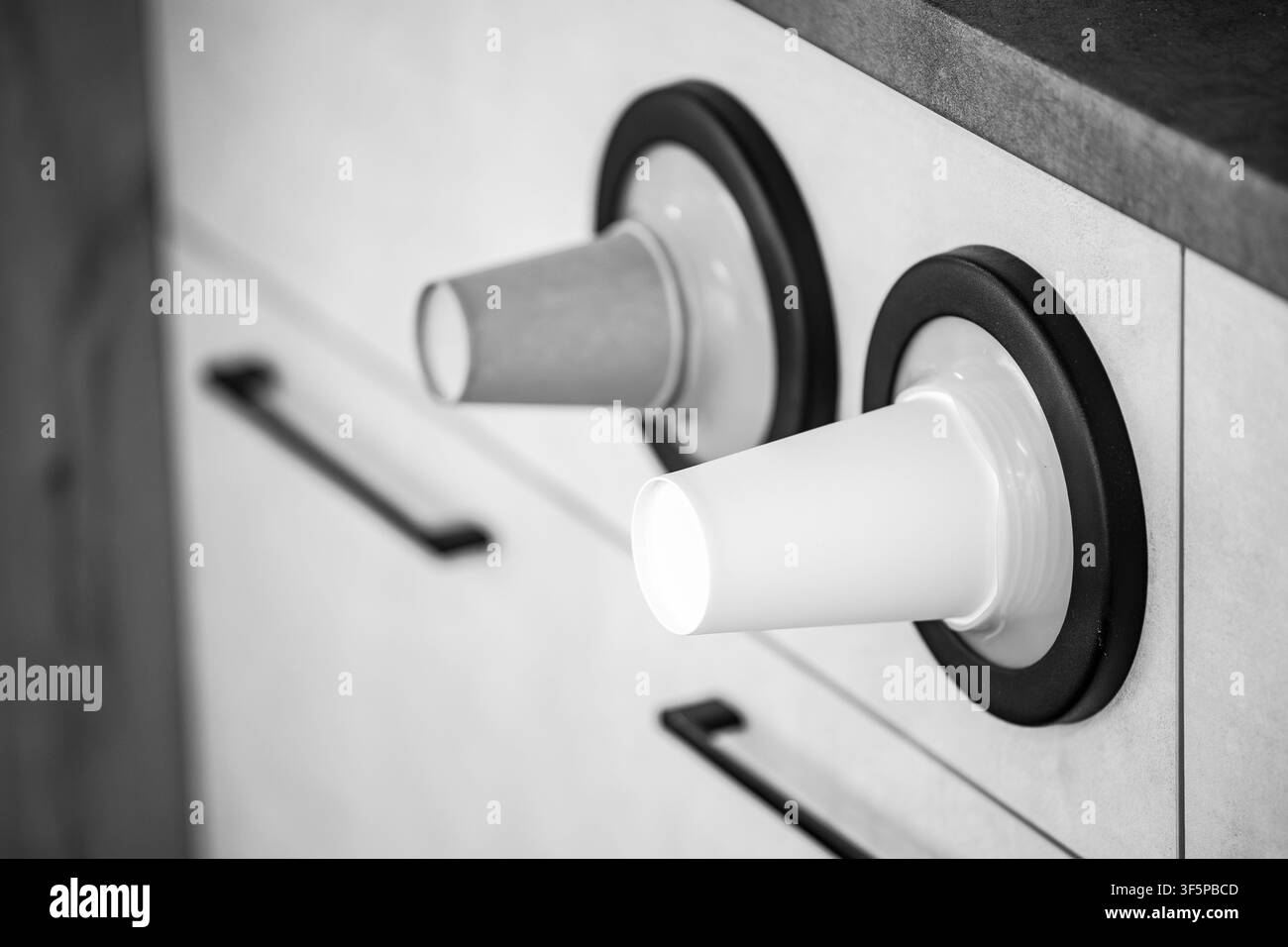 Bicchieri monouso conservati in dispenser circolari montati su mobili da cucina moderni con maniglie scure ed elementi di design minimalista in un Indo luminoso Foto Stock