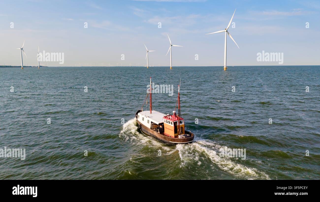 Una vista serena di una barca da pesca che naviga nelle acque del Windmill Park a Espel, Paesi Bassi, circondata da maestose pale eoliche che generano Foto Stock