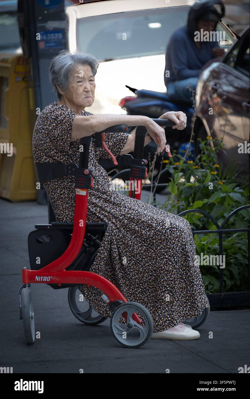 Una donna asiatico-americana anziana e dall'aspetto stanco si riposa sul sedile del suo deambulatore. A Jackson Heights, Queens, New York. Foto Stock