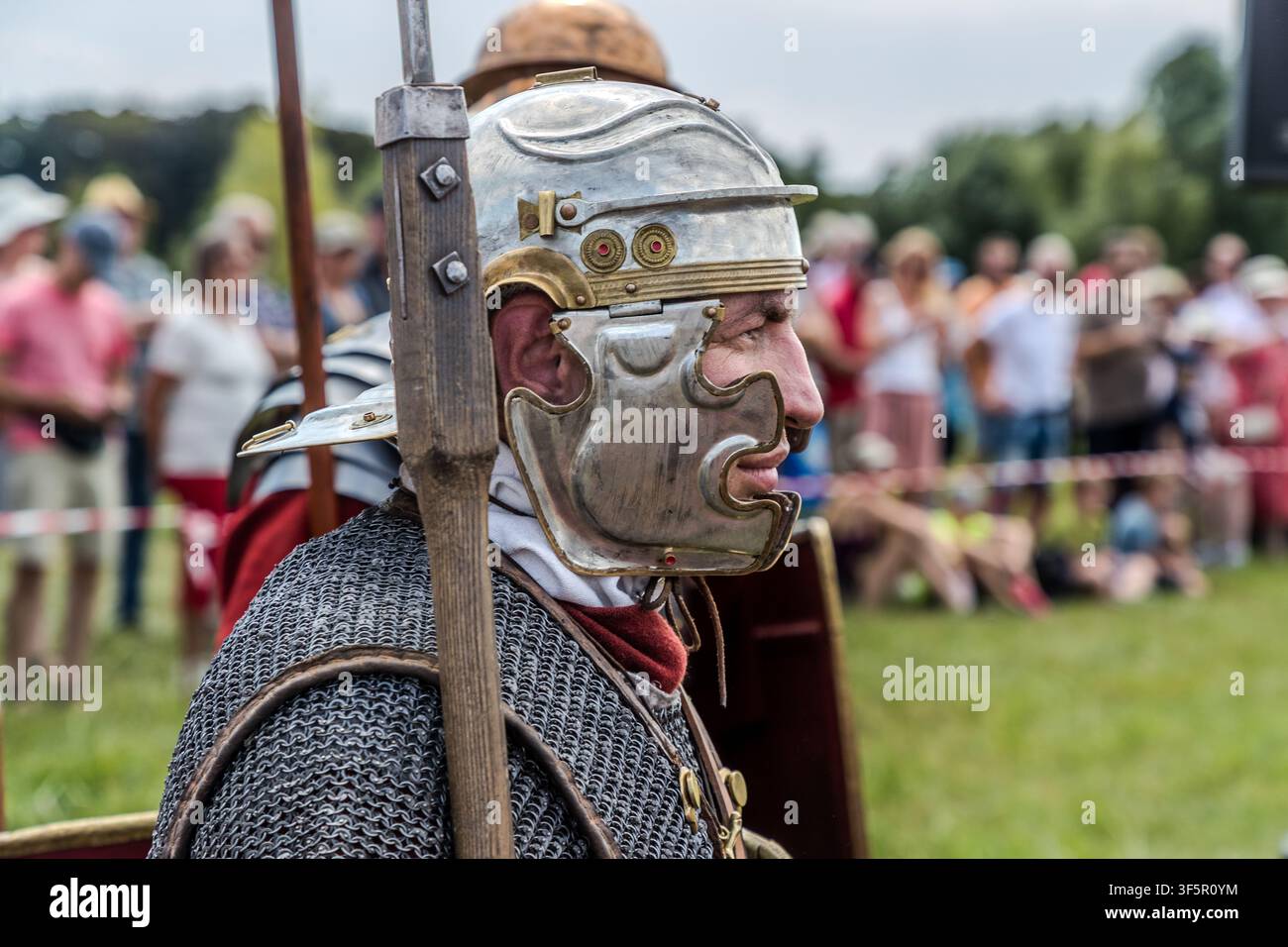 Un legionario di profilo indossa un elmo galea d'argento con protezioni per le guance e una sciarpa rossa, spettatori dietro il nastro di recinzione che osservano la dimostrazione alla mostra gardenica Landesgartenschau (LAGA) a Neuss, Germania. Foto Stock