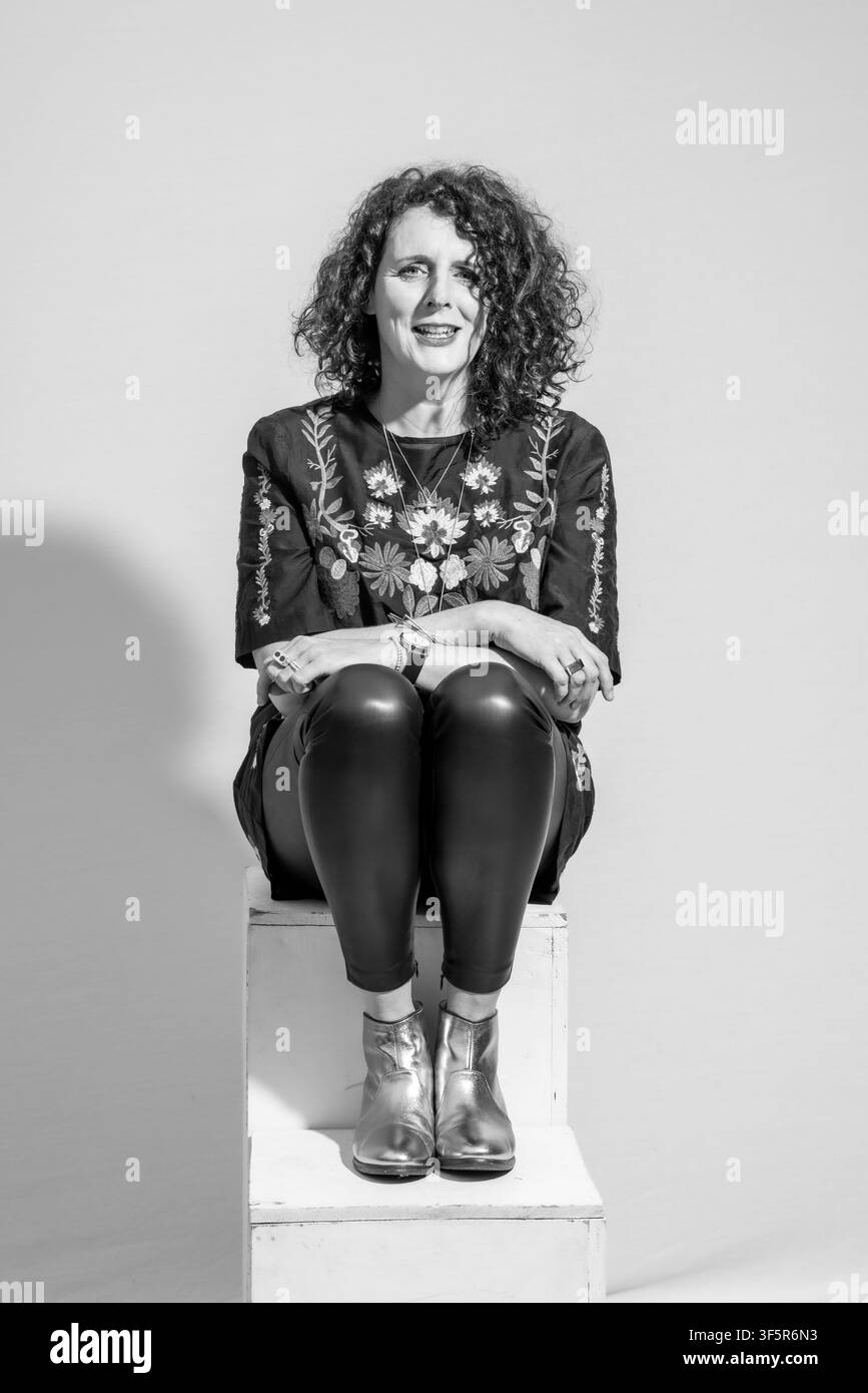 Scrittrice Maggie O'Farrell seduta su una scatola bianca con pantaloni di pelle neri e top floreale Foto Stock
