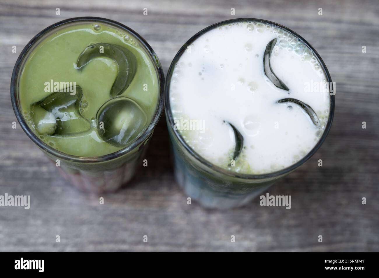 Vista aerea di due bevande ghiacciate al matcha in bicchieri di vetro trasparenti con fette di cetriolo e ghiaccio su un tavolo di legno consumato, che mostra una bevanda schiumosa verde pallido Foto Stock