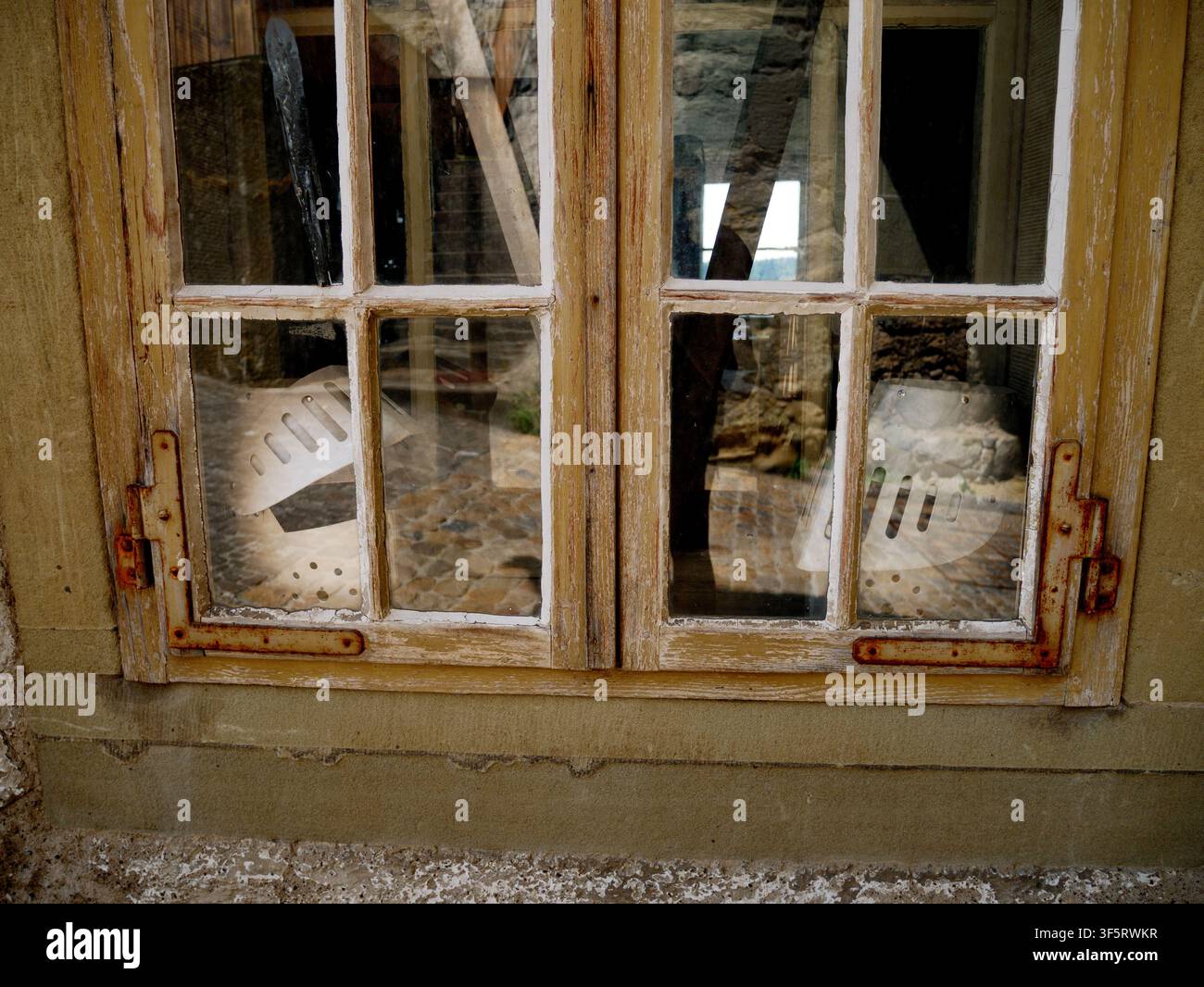 Primo piano di una vecchia finestra di legno con vernice scrostata e cardini arrugginiti Foto Stock