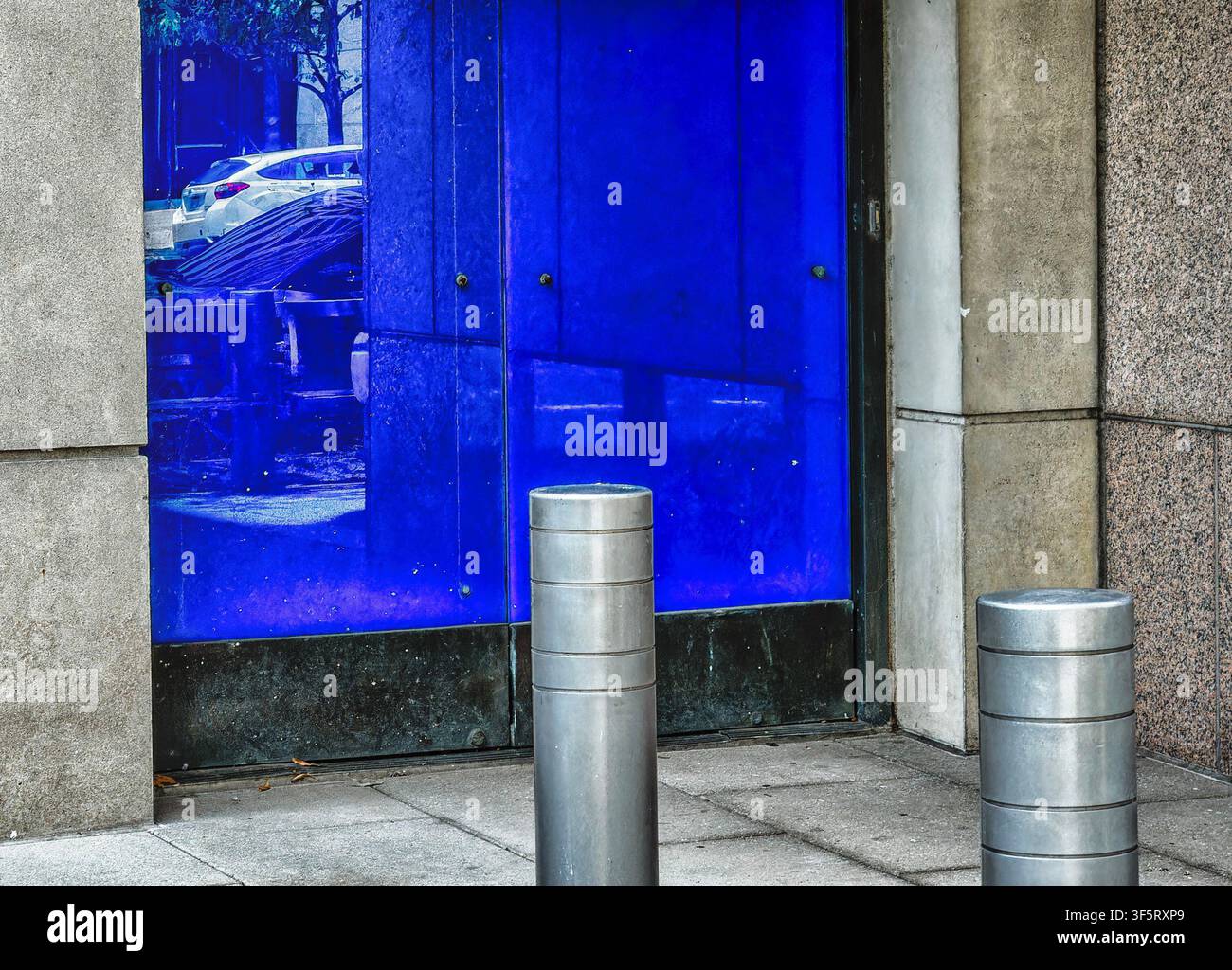 Un BIPA Bollard D100, un pilastro di sicurezza cilindrico davanti a una porta scorrevole blu chiusa Foto Stock