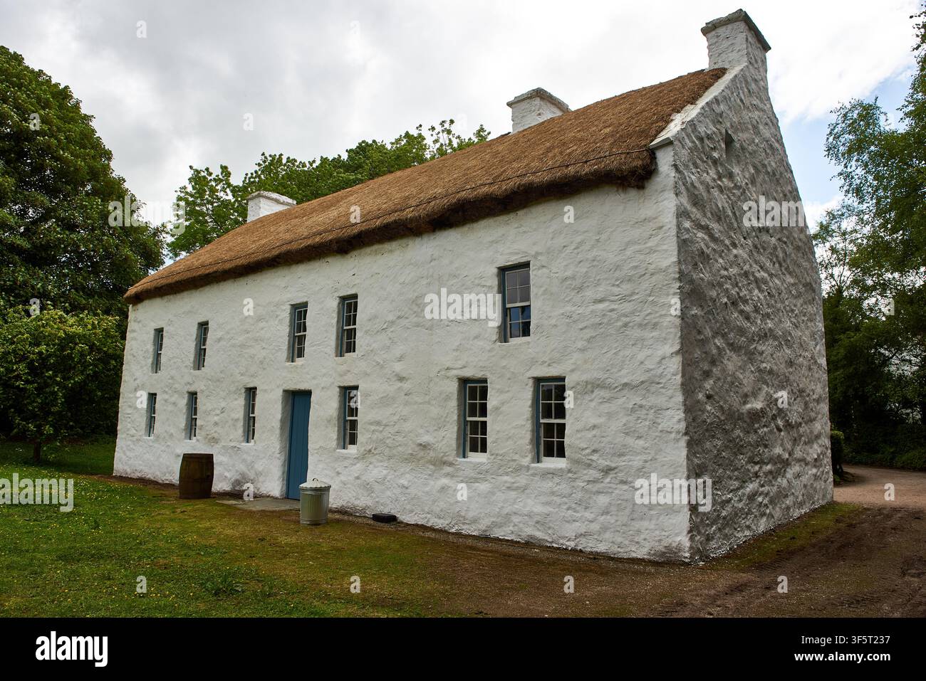 Edificio storico in pietra a due piani con tetto di paglia, porta e finestre blu all'Ulster American Folk Park vicino a Omagh, contea di Tyrone, Irlanda del Nord. Foto Stock