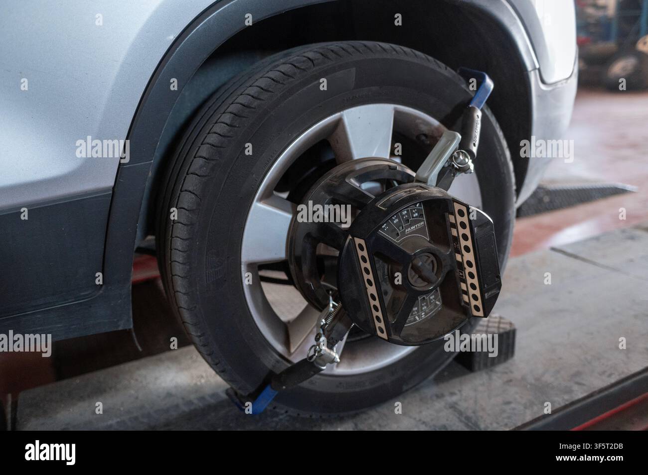 Prima di una ruota di autovettura dotata di sensore di allineamento ruota computerizzato durante l'aggiustamento della sospensione e della geometria dello sterzo in un'officina automobilistica Foto Stock
