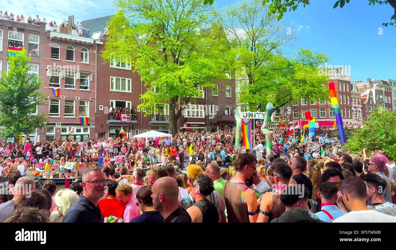 AMSTERDAM, PAESI BASSI - 01 AGOSTO 2026: Una grande folla si raduna vicino al canale accanto a un enorme cartello Unity durante il Pride. Foto Stock