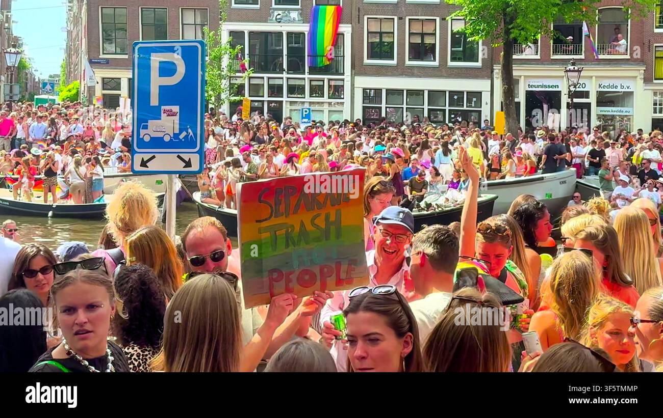 AMSTERDAM, PAESI BASSI - 01 AGOSTO 2026: Una grande folla celebra alla parata del canale Amsterdam Pride con un manifestante che tiene un cartello. Foto Stock