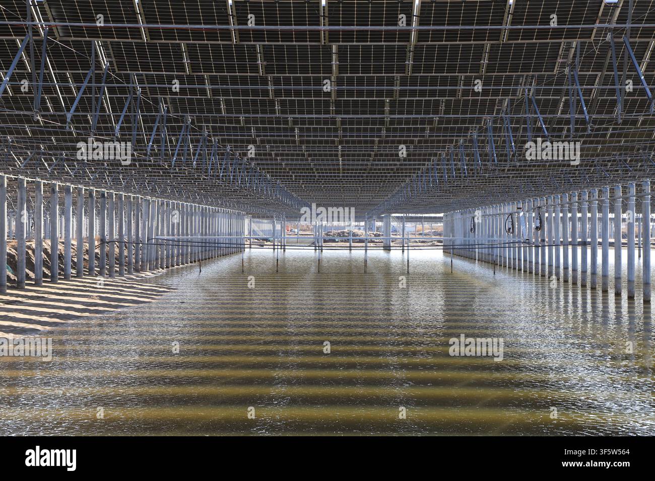 Una vista grandangolare di una centrale fotovoltaica (PV) galleggiante su larga scala, dove i pannelli solari sono montati su supporti metallici sopra la superficie dell'acqua. Foto Stock