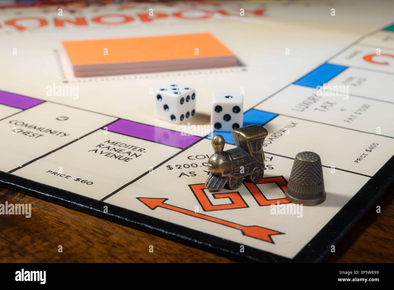 ST. CLOUD, MINNESOTA, STATI UNITI — 27 LUGLIO 2026: Locomotiva in metallo e gettoni per il pollice sullo spazio GO di un tabellone di gioco Monopoly Edizione Nostalgia. Foto Stock