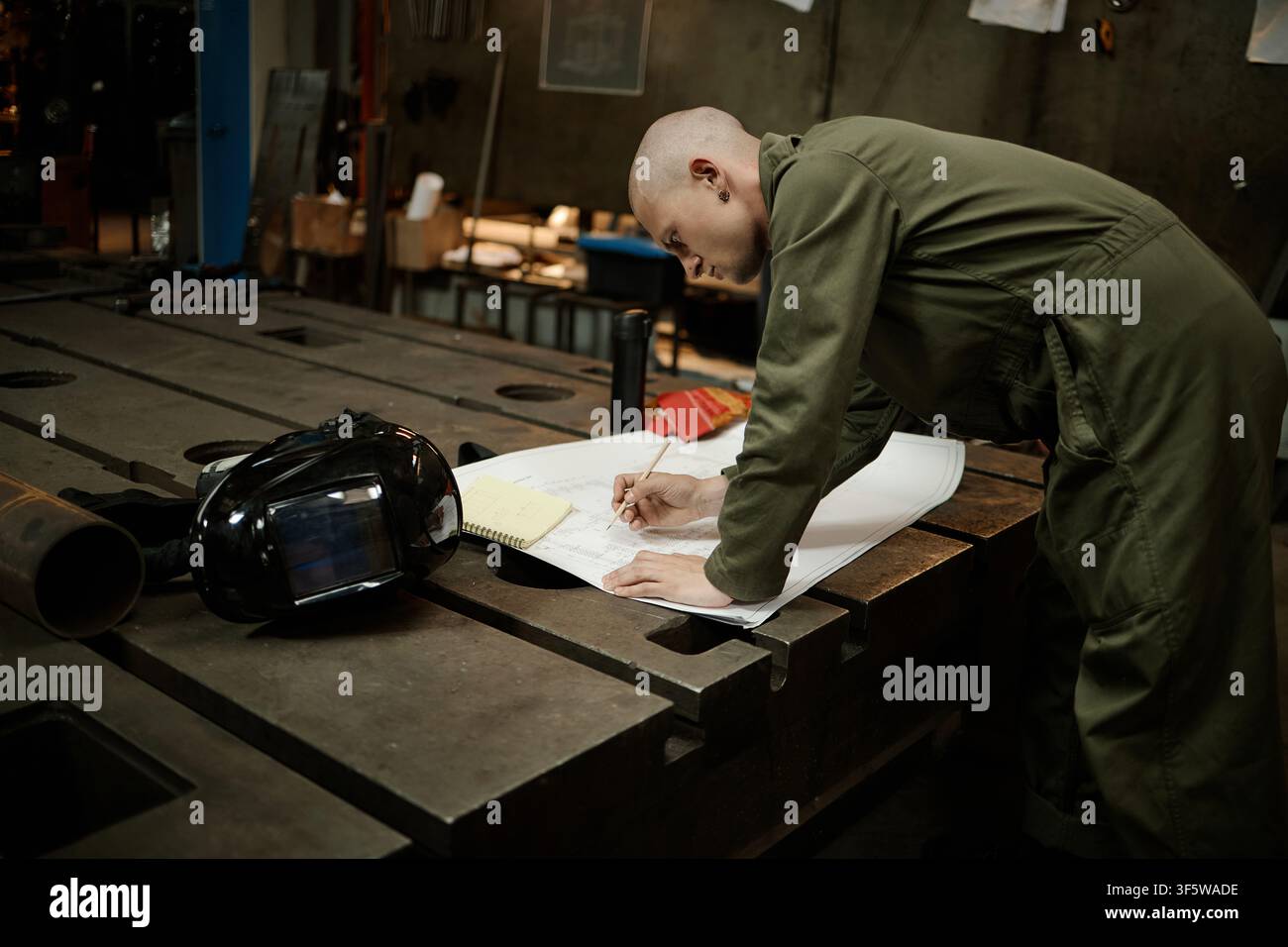 Saldatore maschio che esamina una piantina tecnica su un banco di lavoro in metallo Foto Stock