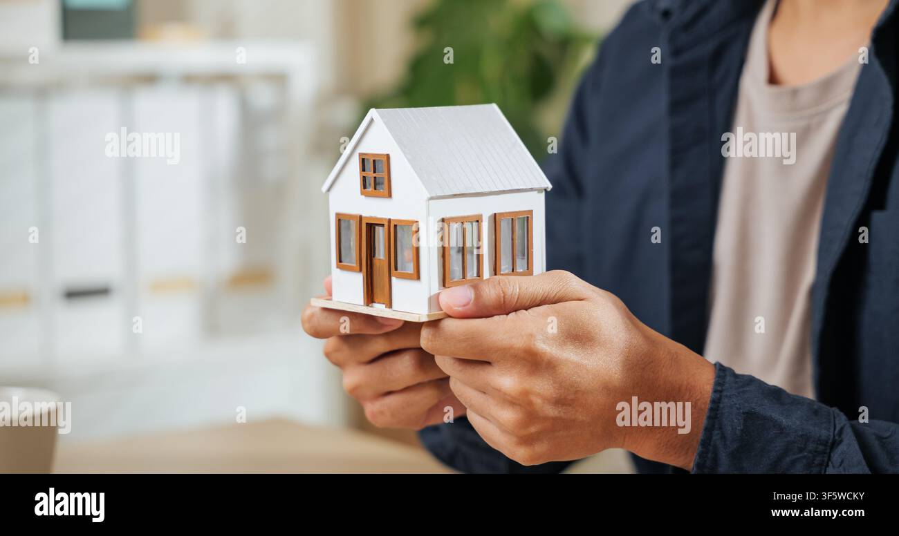 Un agente immobiliare mostra un modello di piccola casa, simboleggiando concetti di proprietà, finanza, mutui e soluzioni abitative. Evidenzia l'agente Foto Stock