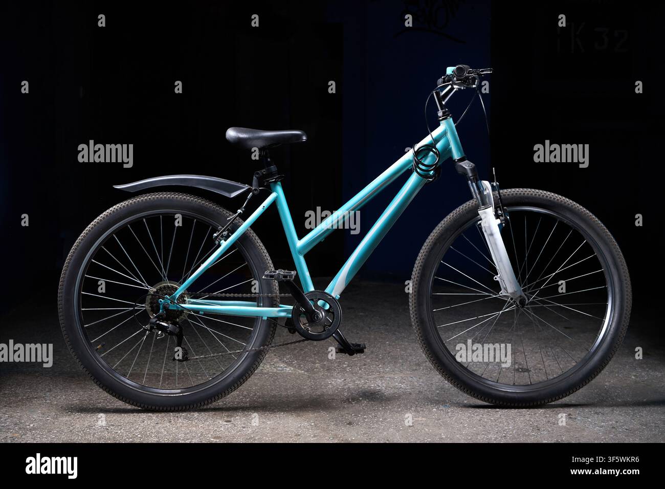 Bicicletta da montagna turchese a passo aperto illuminata in studio su uno sfondo scuro. La bicicletta è dotata di sospensione anteriore, sella nera, parafango posteriore, raggi Foto Stock