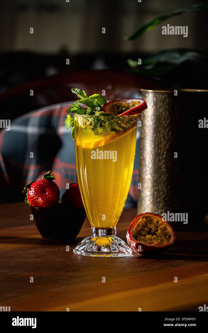 Succo di frutti della passione ghiacciato guarnito con menta fresca e mezze frutti della passione, su un tavolo di legno con fragole e una brocca di metallo incisa. Foto Stock