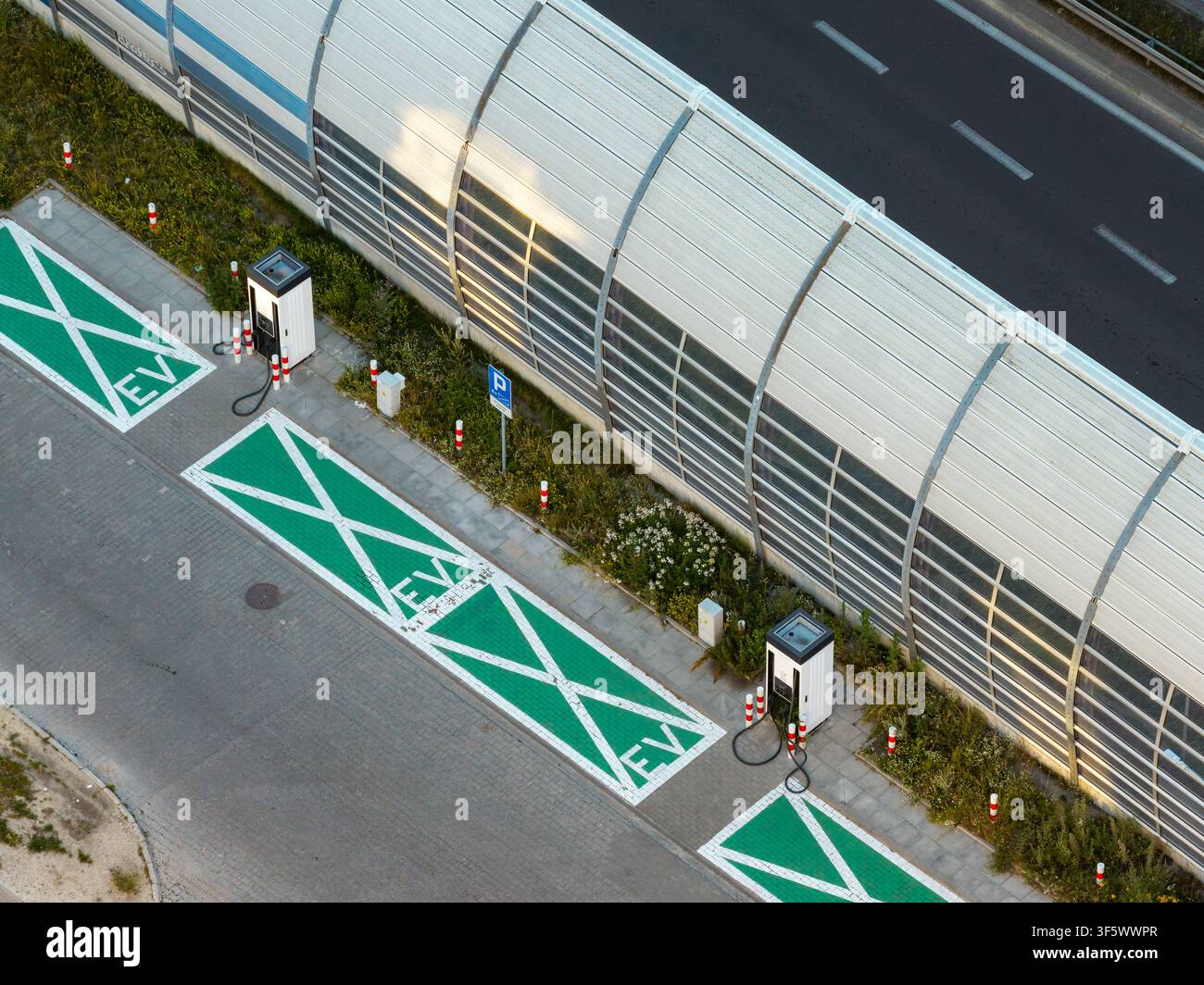 Vista aerea di una stazione di ricarica per auto elettriche con posti parcheggio verdi e punti di ricarica situati lungo un muro antirumore a Varsavia, Voivodato della Masovia Foto Stock