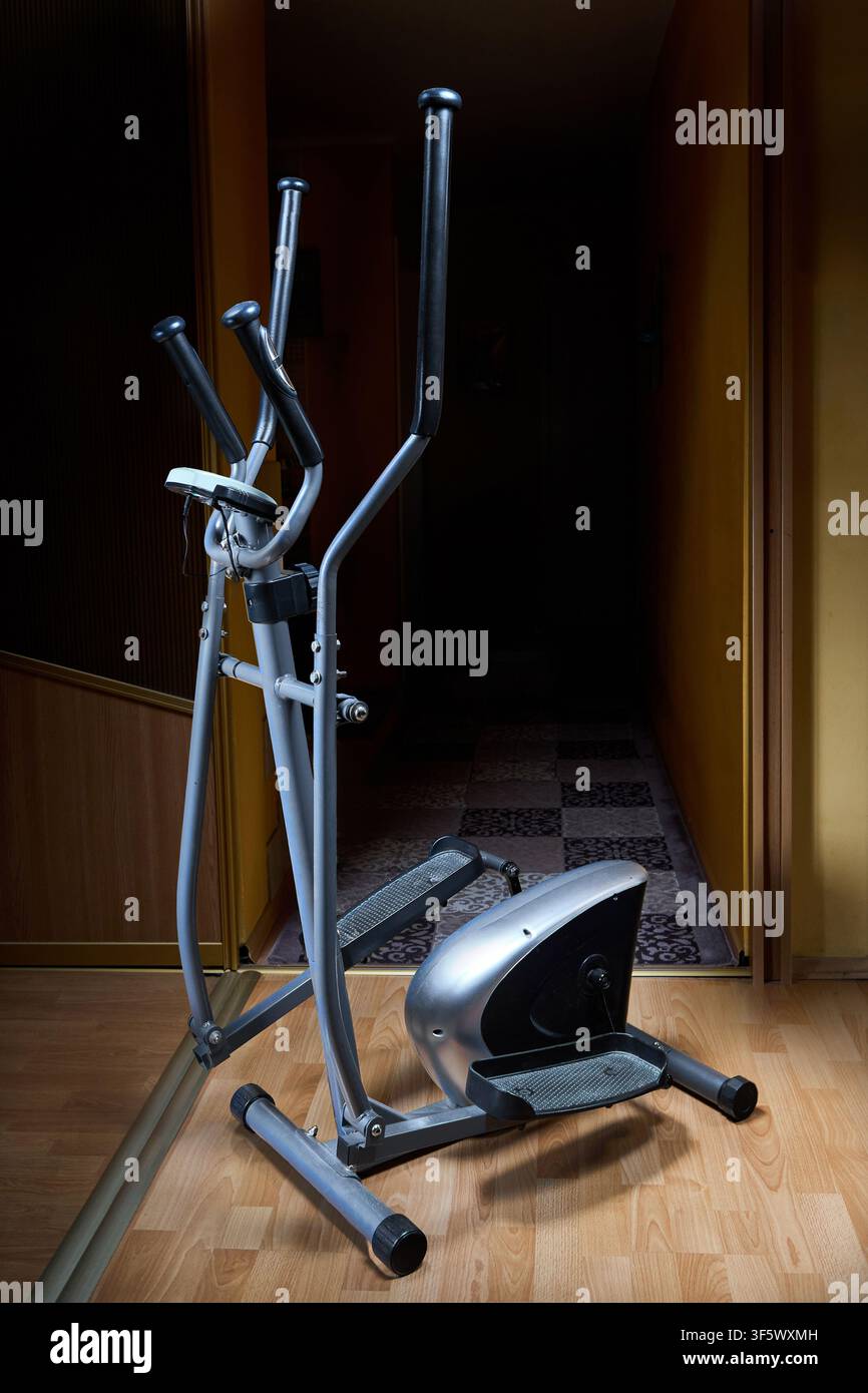 Macchina da esercizio ellittica si trova su pavimento di legno nel corridoio di casa. Il cross trainer magnetico compatto presenta un corpo volano argentato, doppi manubri, Foto Stock