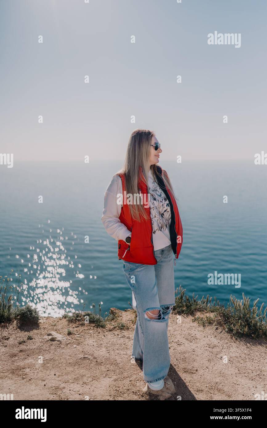 Donna su una scogliera oceanica, in piedi su un bordo roccioso che si affaccia sul vasto mare blu durante una giornata soleggiata con ampio spazio di copia Foto Stock