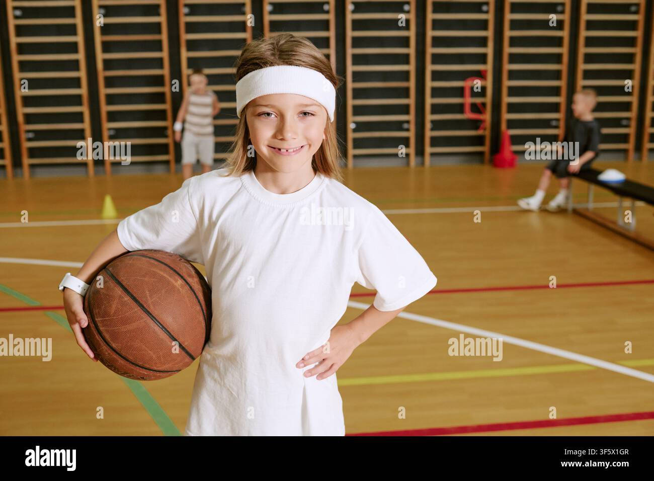 Ritratto di un bambino sorridente che tiene un pallone da basket durante l'allenamento in palestra Foto Stock