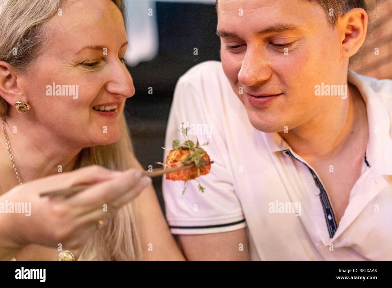 Donna che dà da mangiare sushi a un uomo sorridente in un ambiente accogliente di ristorante. Concetto di sushi giapponese per una coppia a cena e un'esperienza culinaria asiatica romantica. Foto Stock