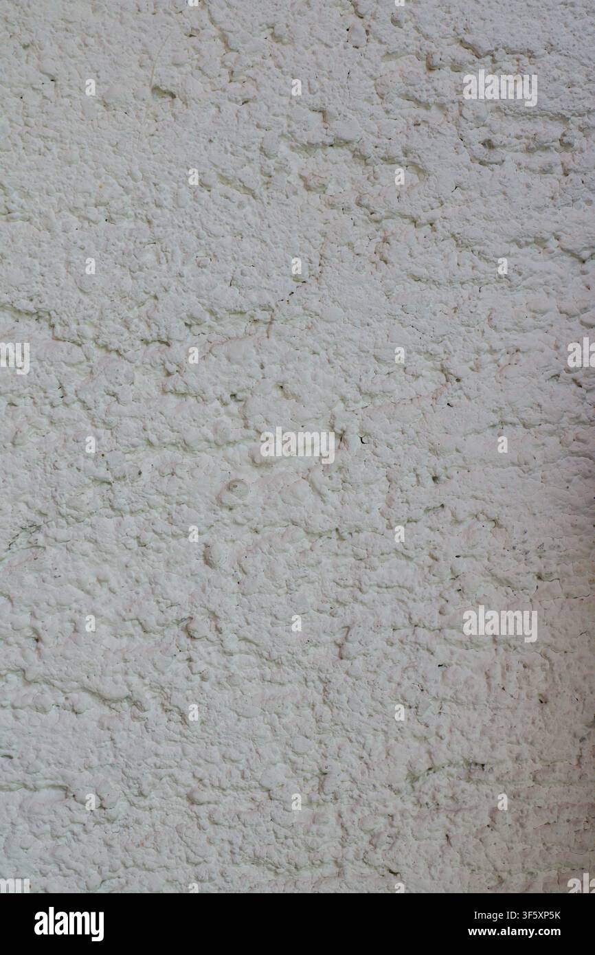 Primo piano di intonaco bianco ruvido con irregolarità pronunciate, struttura porosa e rilievo superficiale naturale Foto Stock