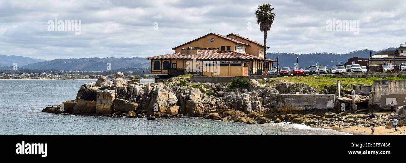 Costa rocciosa ed edificio sul lungomare che si affaccia sulla baia di Monterey sulla costa centrale della California, con l'Oceano Pacifico e le colline circostanti sotto un d Foto Stock