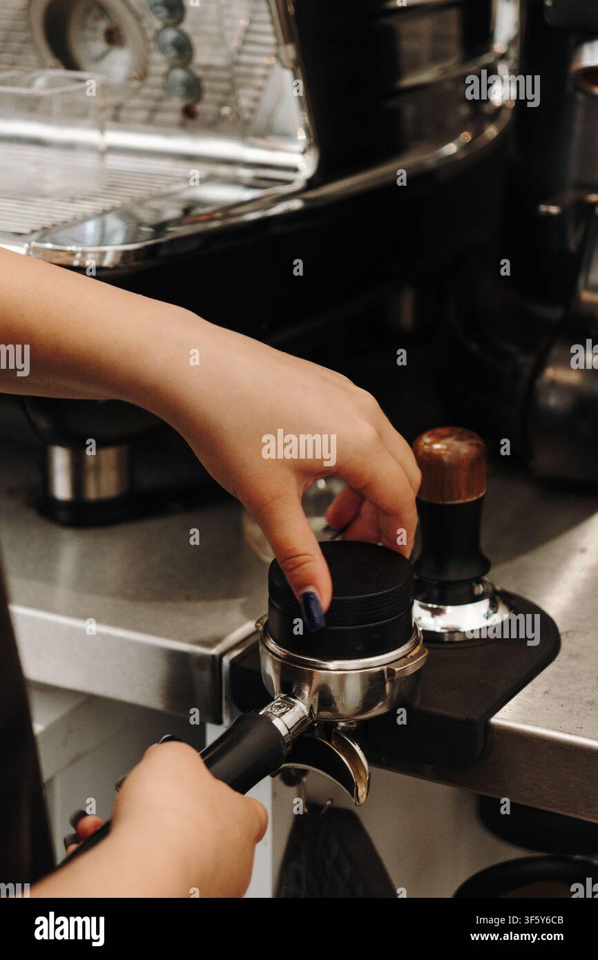 Barista che comprime caffè appena macinato con un tamper prima di preparare l'espresso. Passo essenziale nella preparazione del caffè speciale. Foto Stock