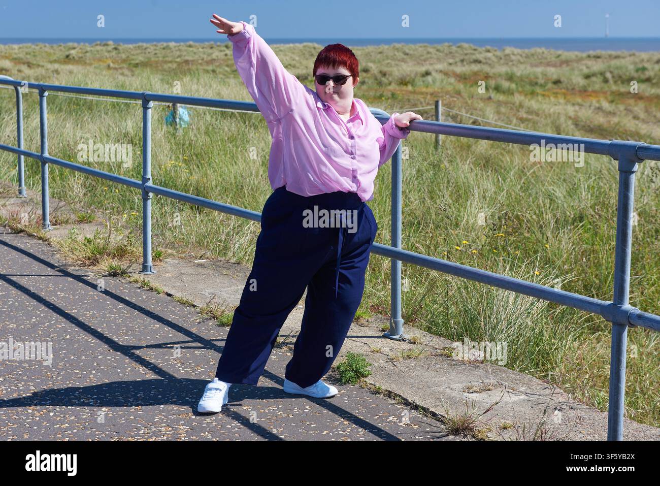 Attrice con sindrome di Down che tende il braccio sollevato sulla promenade di Great Yarmouth durante le riprese del cortometraggio Still Here, commissionato da Compass Dance Foto Stock